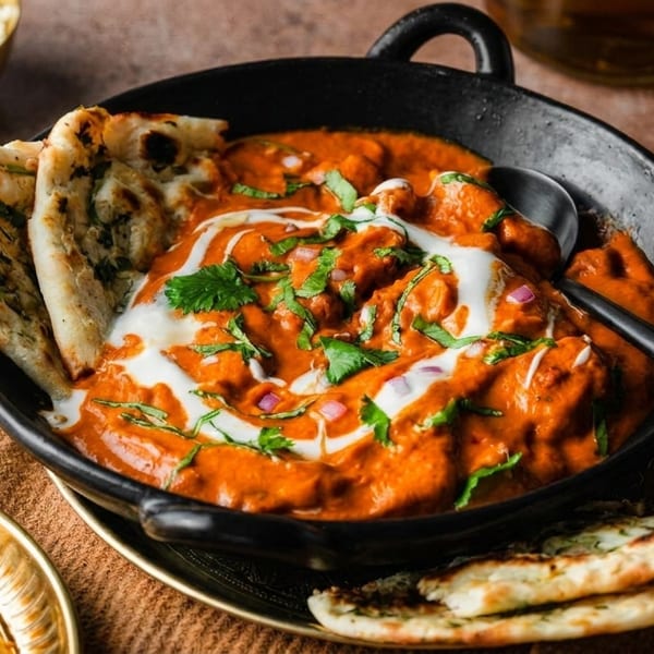Butter chicken with naan bread, rice, and samosas on a rustic table.